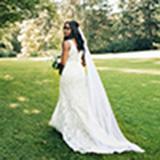 Beautiful bride stands in a lush green field adorned in a stunning white lace wedding dress. Captured by wedding photographer