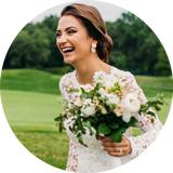 In Vancouver, a bride stands surrounded by a circle of flowers, wearing a white dress and holding a bouquet. Her joyful smile complements the serene outdoor setting, possibly in a field or garden. Earthy tones dominate, with green and beige hues accentuating the scene. Captured by wedding photographer Andrew Bidylo, the image radiates a joyful and serene mood, perfect for weddings.