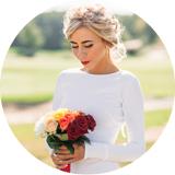 A stunning photo captured in Vancouver by wedding photographer Andrew Bidylo, depicting a woman in a beautiful white wedding dress standing gracefully. She holds a bouquet of flowers, prominently featuring vibrant roses.